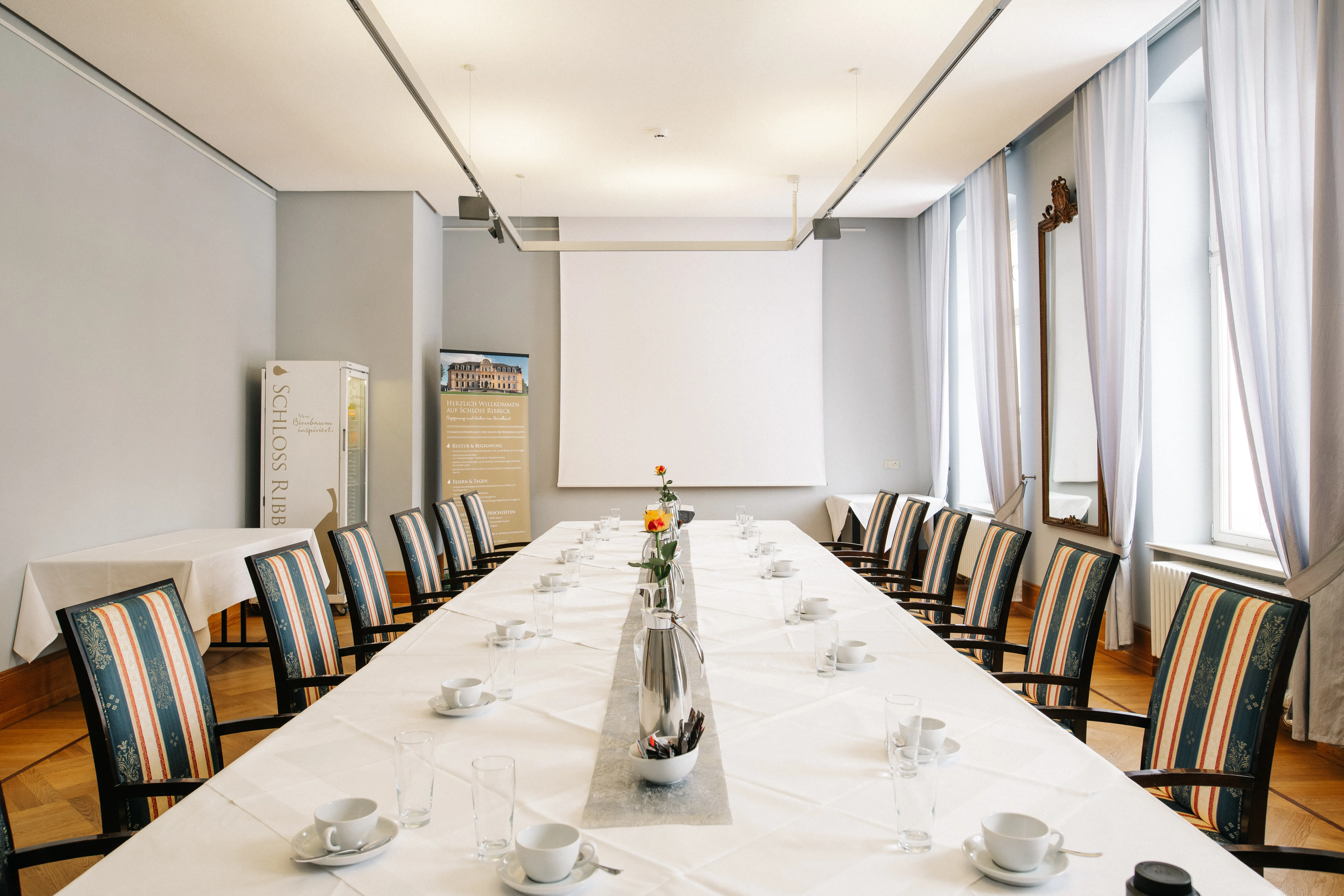 Konferenzraum auf Schloss Ribbeck mit langer Tischreihe und Leinwand